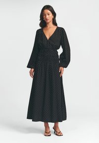Černé maxi šaty s bílými puntíky, mají dlouhé rukávy, hluboký V-výstřih a nařasený pas pro přiléhavý vzhled. Jemný textilní materiál.