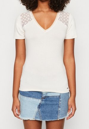 T-shirt blanc en coton avec un col en V, décoré d'accents en dentelle sur les épaules. Manches courtes et coupe ajustée complètent le style.