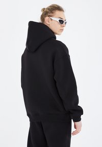 Black hooded sweatshirt with a relaxed fit, featuring ribbed cuffs and hem. Smooth texture and minimalistic design, shown from the back.