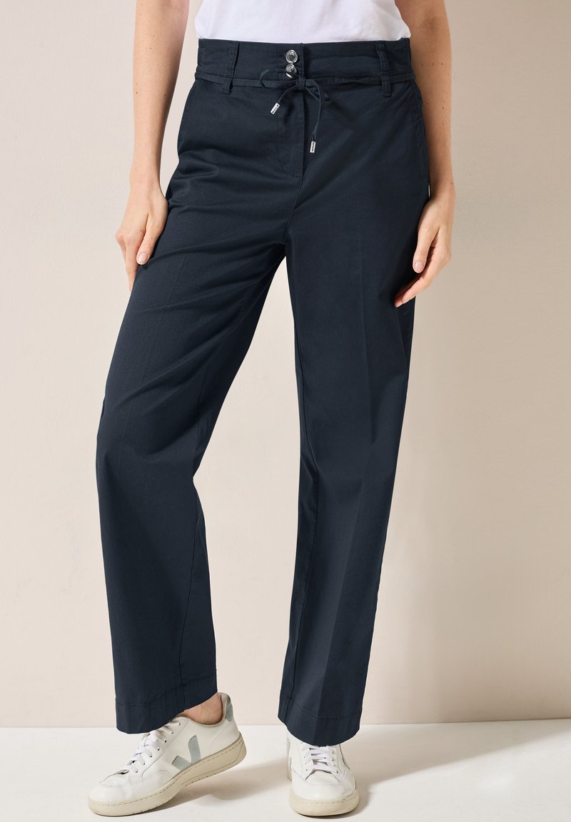 Marineblauwe wijde broek met een trekkoord taille en knoopsluiting, gemaakt van zachte stof. Gecombineerd met witte sneakers met grijze accenten.