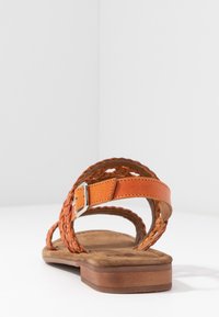 Orange leather sandal with woven strap design, flat brown sole, adjustable ankle buckle, and a soft textured footbed.