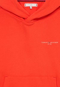 Czerwona bluza z kapturem wykonana z mieszanki bawełny. Posiada przednią kieszeń oraz białe logo 'Tommy Hilfiger' po lewej stronie. Gładka faktura.