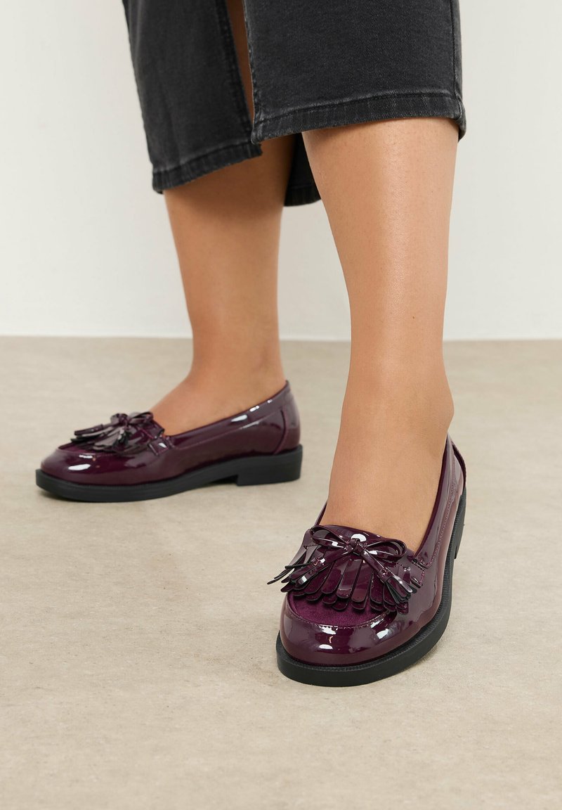 Burgundy patenterade läderskor med rund tå, dekorativt frans och rosettdetalj, som har en låg svart gummihäl. Slät yta.