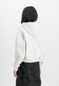 Hoodie cropped grigio chiaro con cappuccio regolabile e polsini a coste. Indossato con una gonna nera con tasca laterale e dettagli di cucitura.