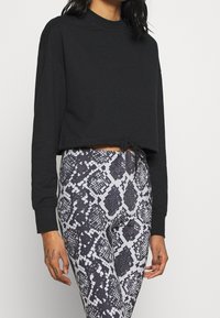 Felpa nera cropped con maniche lunghe e coulisse all'orlo, abbinata a leggings a vita alta con motivo pitonato grigio e nero.