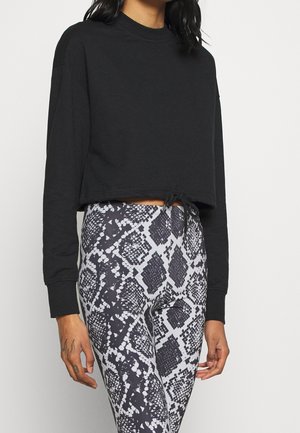 Svart kort sweatshirt med långa ärmar och dragsko i nederkant, kombinerad med högmidjade leggings i ett grått och svart ormskinsmönster.