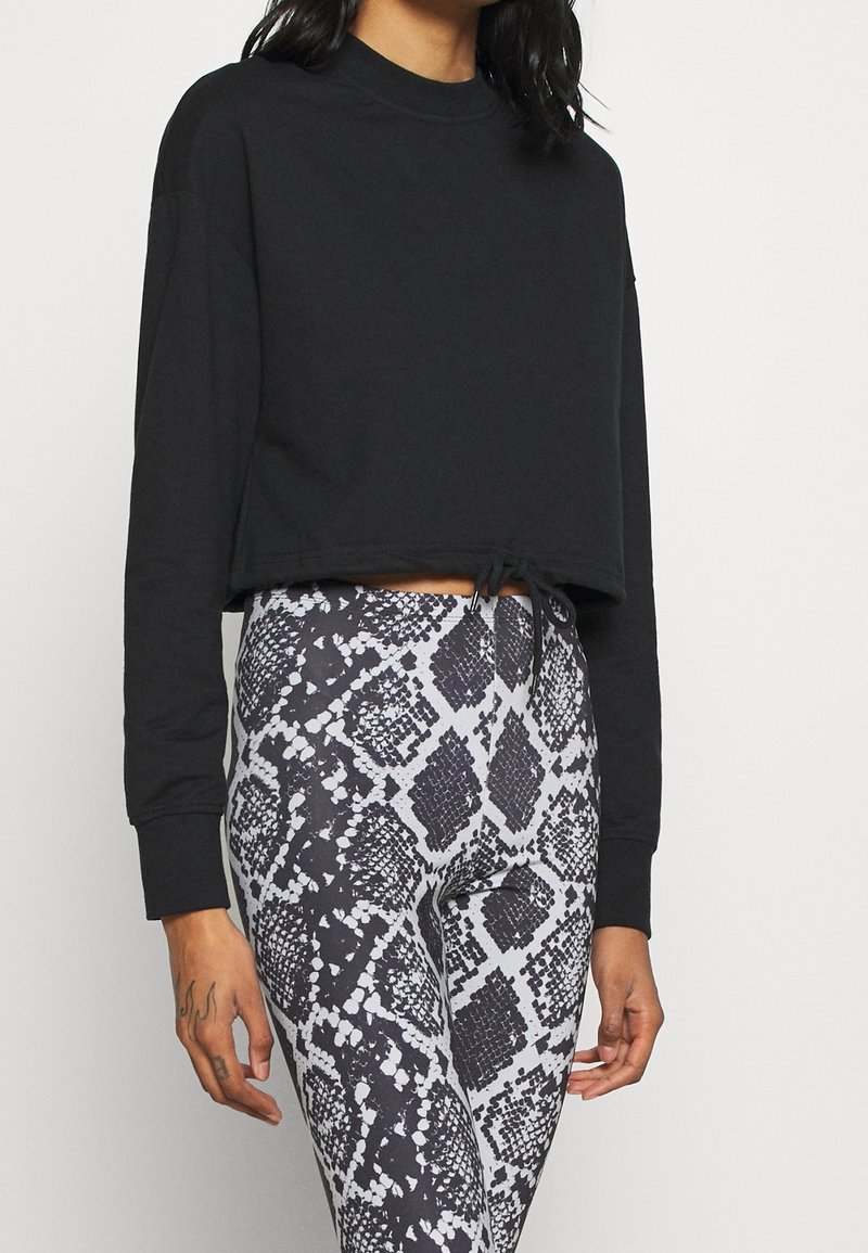 Felpa nera cropped con maniche lunghe e coulisse all'orlo, abbinata a leggings a vita alta con motivo pitonato grigio e nero.