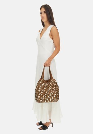 Borsa intrecciata marrone e crema con due manici marroni. La borsa ha una forma morbida e una superficie texturizzata. Il modello indossa un lungo vestito bianco e tacchi neri.