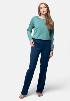 Lichtblauw langemouw shirt met een ronde hals, gecombineerd met donkerblauwe, geribbelde, elastische broek met tailleband. Model staat op blote voeten.