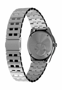 Montre en acier inoxydable argenté Timex avec un bracelet à maillons, des maillons hexagonaux et un boîtier arrière rond. Elle possède un logo gravé sur le fermoir.