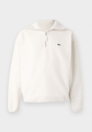 White fleece pullover with a half-zip collar, soft texture, ribbed collar, and a small green logo on the left chest area.