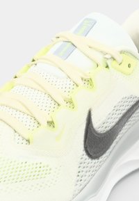Baskets de sport légères en maille blanche et jaune pâle. Présentent un logo gris, des accents jaunes, des lacets plats et une tige texturée.