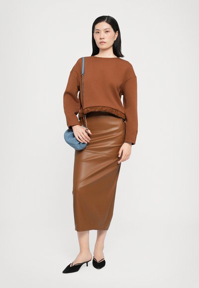 Hnědá zkrácená mikina s volánkovým lemem, hnědá lesklá kožená midi sukně a modrá tkaná kabelka. Černé muly s špičatou špičkou dotvářejí celkový vzhled.