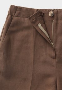 Brown linen pants with elastic waistband, half unzipped zipper, and dual contrasting buttons on the front closure.