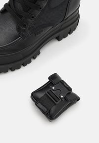Botte en cuir noir avec un dessus texturé, embout rond et semelle épaisse, accompagnée d'une petite pochette en cuir noir dotée d'une boucle et d'une sangle.