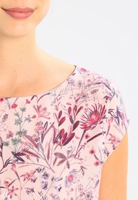 Haut à motifs floraux avec des manches courtes, présentant une couleur de base rose et diverses fleurs dans des nuances de rouge, de violet et de vert, avec une texture lisse.