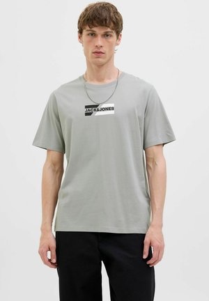 Light grey cotton T-shirt with short sleeves, featuring a black and white logo print on the front. Smooth texture, relaxed fit.