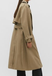 Beżowy trencz z paskiem w talii, ramionami w stylu peleryny i długimi rękawami. Wykonany z gładkiego materiału, ma luźny krój.