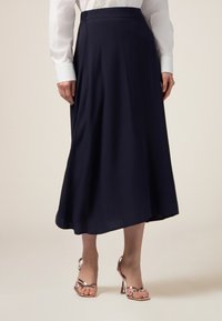 Une jupe midi fluide en bleu marine, en tissu doux avec une texture lisse, associée à des sandales à talons hauts dorées rose avec des lanières.