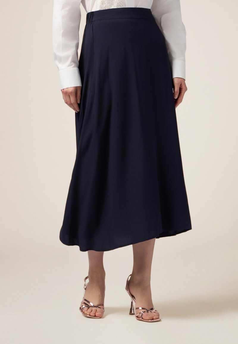 Une jupe midi fluide en bleu marine, en tissu doux avec une texture lisse, associée à des sandales à talons hauts dorées rose avec des lanières.