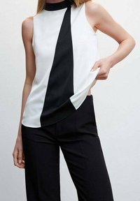 Haut sans manches avec un col haut, un bloc de couleur blanc et noir, et une texture lisse. Associé à un pantalon noir ajusté.