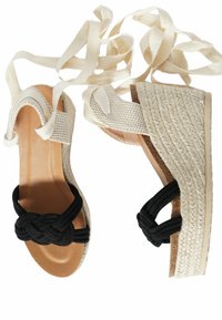 Sandali intrecciati neri con design a fascia annodata, suola espadrilla beige e lacci per la caviglia in tela regolabili. Plantare in pelle liscia.