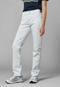 Pantalones vaqueros de denim blanco con un diseño ajustado, estilo de cinco bolsillos y una textura suave, combinados con zapatillas deportivas grises.