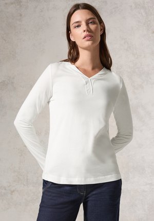 Maglietta bianca a maniche lunghe con scollatura a V, in morbido cotone, dal tessuto liscio, design semplice, indossata con jeans blu scuro.