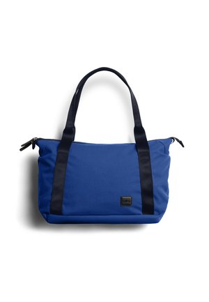 Sac cabas bleu avec poignées noires et fermeture éclair, écusson logo rectangulaire à l'avant, fond uni.