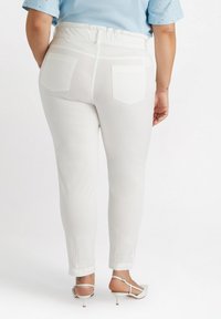 Pantalones ajustados blancos con una cinturilla elástica, que cuentan con dos bolsillos traseros. Se combinan con sandalias de tacón alto de color claro.