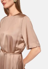 Beige satin dress with short sleeves, a round neckline, and a tied waist. Features smooth texture and subtle sheen.
