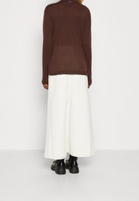 Brun långärmad topp i ett lätt material, kombinerad med en vit, knälång kjol och svarta kraftiga stövlar. Enkelt design med minimala accenter.