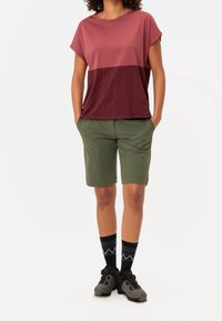 Camisa de manga corta en bloques de color en tonos de rosa, combinada con pantalones cortos verdes. Calcetines negros con patrón geométrico blanco y calzado gris.