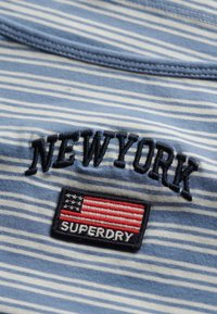 Blau-weiß gestreiftes Hemd mit besticktem "NEWYORK"-Text und einem Patch mit einer amerikanischen Flagge und "SUPERDRY" in Schwarz. Weicher Stoff.