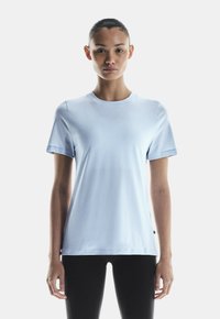 Világoskék, rövid ujjú póló sima anyagból. Kerek nyakú dizájn, minimális varrásokkal és egyenes szegéllyel. Fekete leggings-el párosítva.