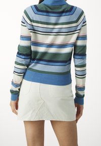 Flerfärgad randig tröja i gröna, blå och rosa nyanser med hög krage och ribbade muddarna, tillsammans med en vit kort kjol.