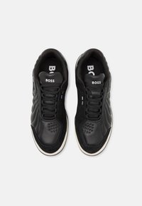 Une paire de baskets noires BOSS avec des panneaux en cuir et en daim, un système de laçage à l'avant et un logo blanc sur la languette rembourrée, présentée de dessus sur fond blanc.