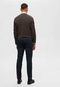 Herrklädsel som består av en mörkbrun tröja, marinblåbyxor och svarta skor. Tröjan har rundad halsdesign och långa ärmar.