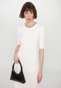 Robe en maille côtelée blanche à manches courtes, associée à un sac à main noir en relief crocodile avec une poigne incurvée et une fermeture éclair dorée.