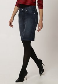 Mörk denimpennkjol med en figurnära design, femficksstil och kontrastsömmar. Bärs med svarta strumpbyxor och högklackade skor.