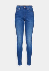 Jeans ajustados en denim azul medio, con una cintura alta, cinco bolsillos, cremallera frontal y costuras contrastantes. Textura suave en toda la prenda.