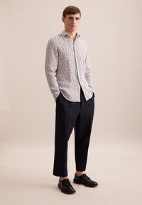 Wit shirt met lange mouwen en een bloemenpatroon, marineblauwe broek en zwarte leren schoenen; slim fit, met knoopsluiting en rechte pijpen.
