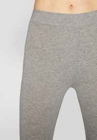 Leggings gris avec une texture lisse, une taille élastique et un design ajusté. Tissu tricoté en machine sans motifs ni accents visibles.
