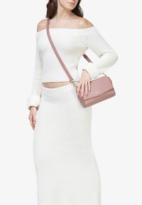 Suéter blanco de punto acanalado sin hombros y falda a juego, combinado con un pequeño bolso cruzado rosa con tapa y herrajes dorados.