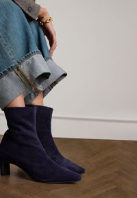 Marineblaue Wildleder-Stiefeletten mit spitzem Zehenbereich und Blockabsatz, kombiniert mit einem Denim-Rock mit ausgefranstem Saum und kontrastierenden Nähten.