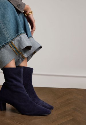 Bottines en daim bleu marine à bout pointu et talon carré, associées à une jupe en denim avec un ourlet effiloché et des coutures contrastées.