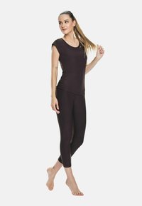 Top atletico aderente marrone scuro con maniche corte e scollatura a barchetta, abbinato a leggings tre quarti coordinati. Texture liscia e design elegante.
