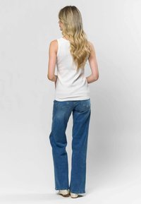 Bela rebrasta majica na bretele v kombinaciji z visokim modrim džinsom. Džinsi imajo klasičen kroj z žepi in sproščen fit.