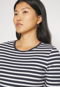 Top a rayas en azul marino y blanco con cuello redondo y mangas largas, fabricado en una tela suave, que presenta una forma ajustada y una textura lisa.