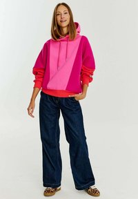 Módní mikina ve fuchsiové a růžové barvě s kapucí na šňůrky a volným střihem, v kombinaci s tmavě modrými širokými džíny a teniskami se zvířecím potiskem.